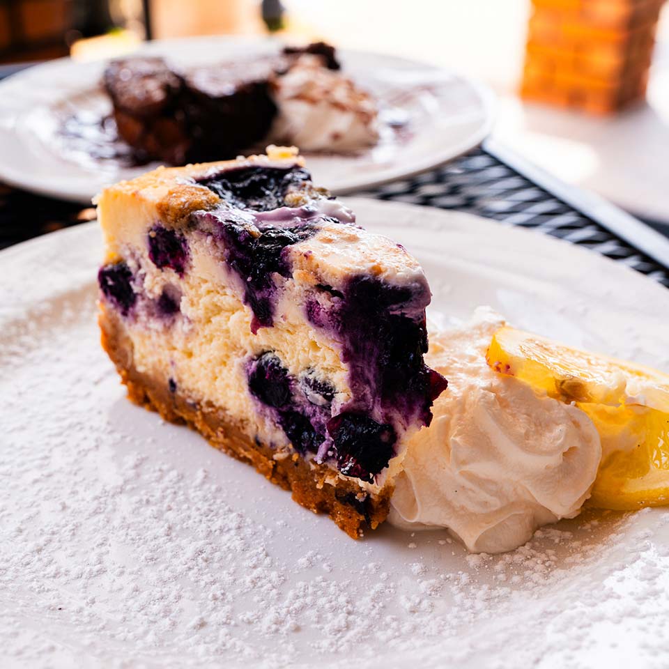 Slice of blueberry cheesecake with whipped cream at DeBlaze at 131, garnished on a white plate.