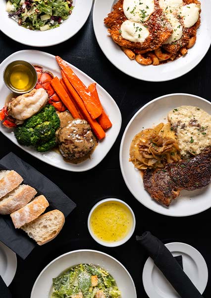 A variety of plated dishes at this steakhouse, featuring steak, chicken, veggies, and fresh bread.