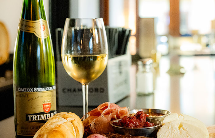 A glass of white wine, bread, meats, and cheese on a table at an Italian steakhouse.