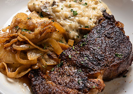 Grilled steak with sautéed onions and creamy mashed potatoes, served at Carnegie Restaurant.