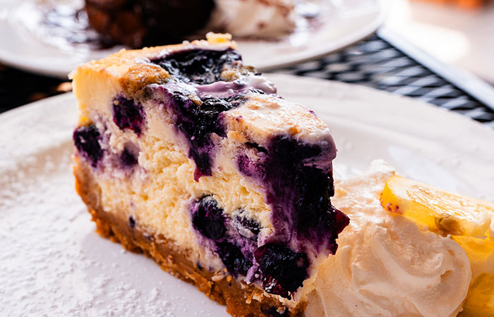 A slice of blueberry cheesecake at DeBlaze at 131, with crumb crust and whipped cream on a plate.