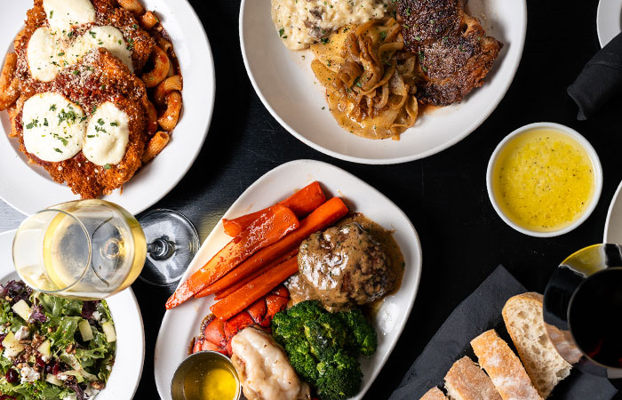 Plates of assorted dishes at Carnegie Italian restaurant: veggies, bread, salad, wine, and sauces.