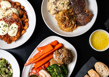 Enjoy meals at DeBlaze at 131: steak, chicken, veggies & salad on white plates at a black table.
