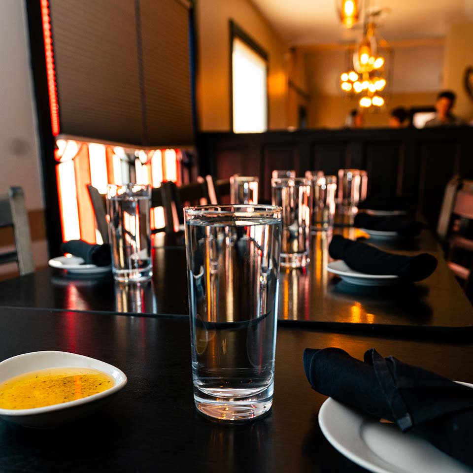 A row of glasses and black napkins on a polished Italian restaurant table, softly lit.