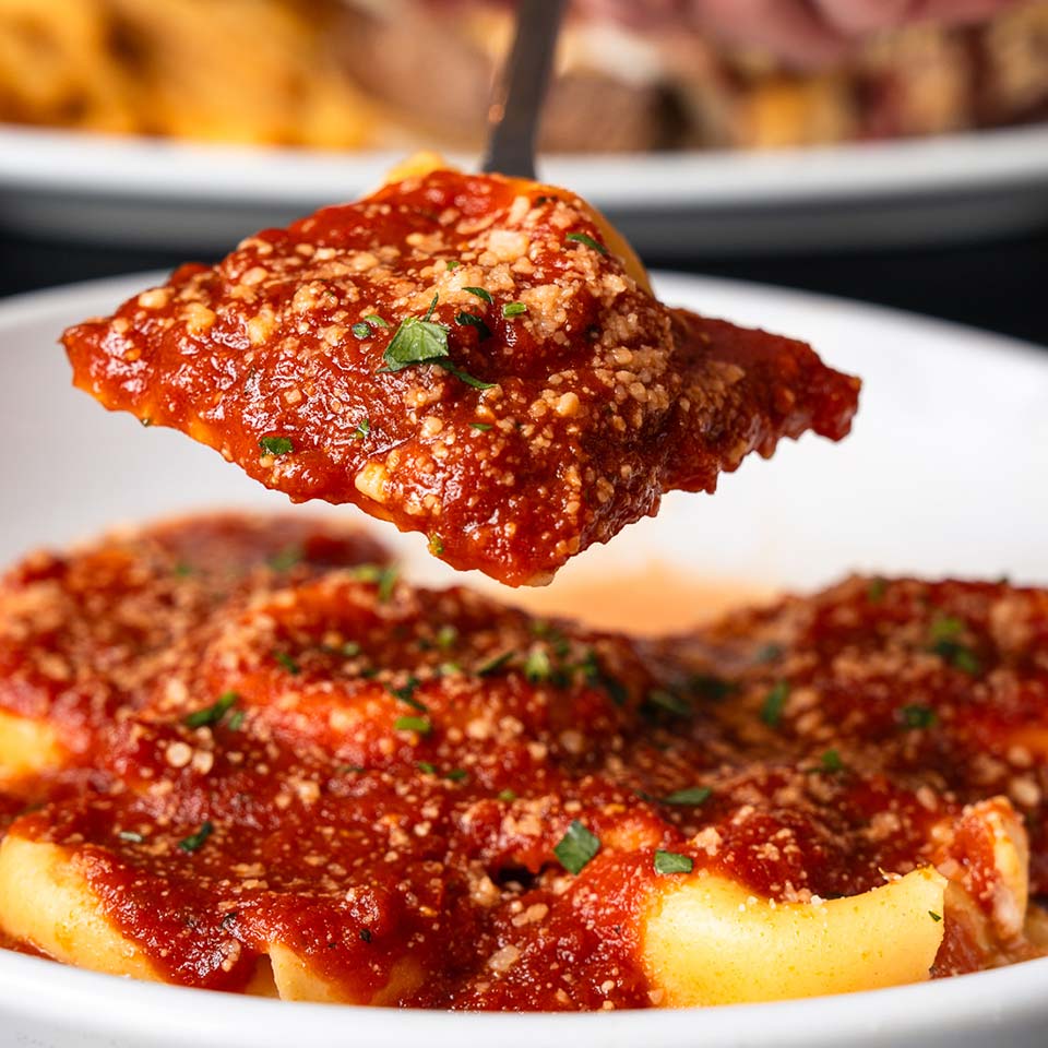 A fork holds pasta with tomato sauce at DeBlaze at 131 above a bowl filled with more pasta.