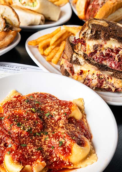 Ravioli with red sauce, fries, and a stacked sandwich at Carnegie Restaurant on a dining table.