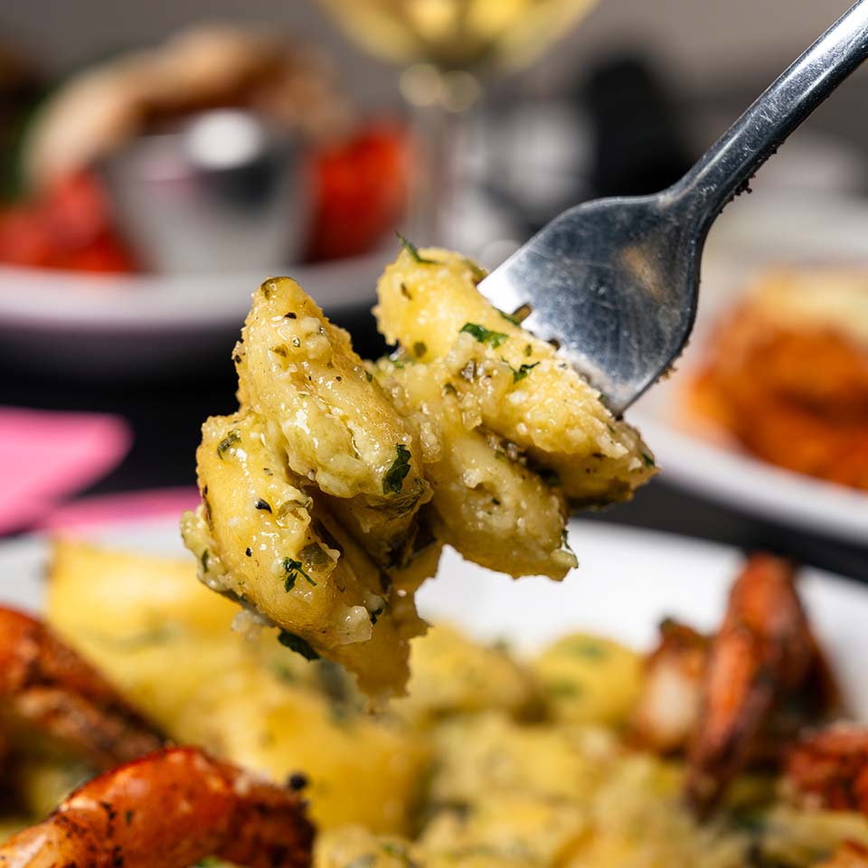 A fork holds gnocchi with herbs and cheese at this Italian steakhouse, seafood in the background.