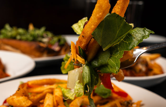 A fork holds fries, lettuce, and veggies above Italian dishes at a vibrant steakhouse and bar.