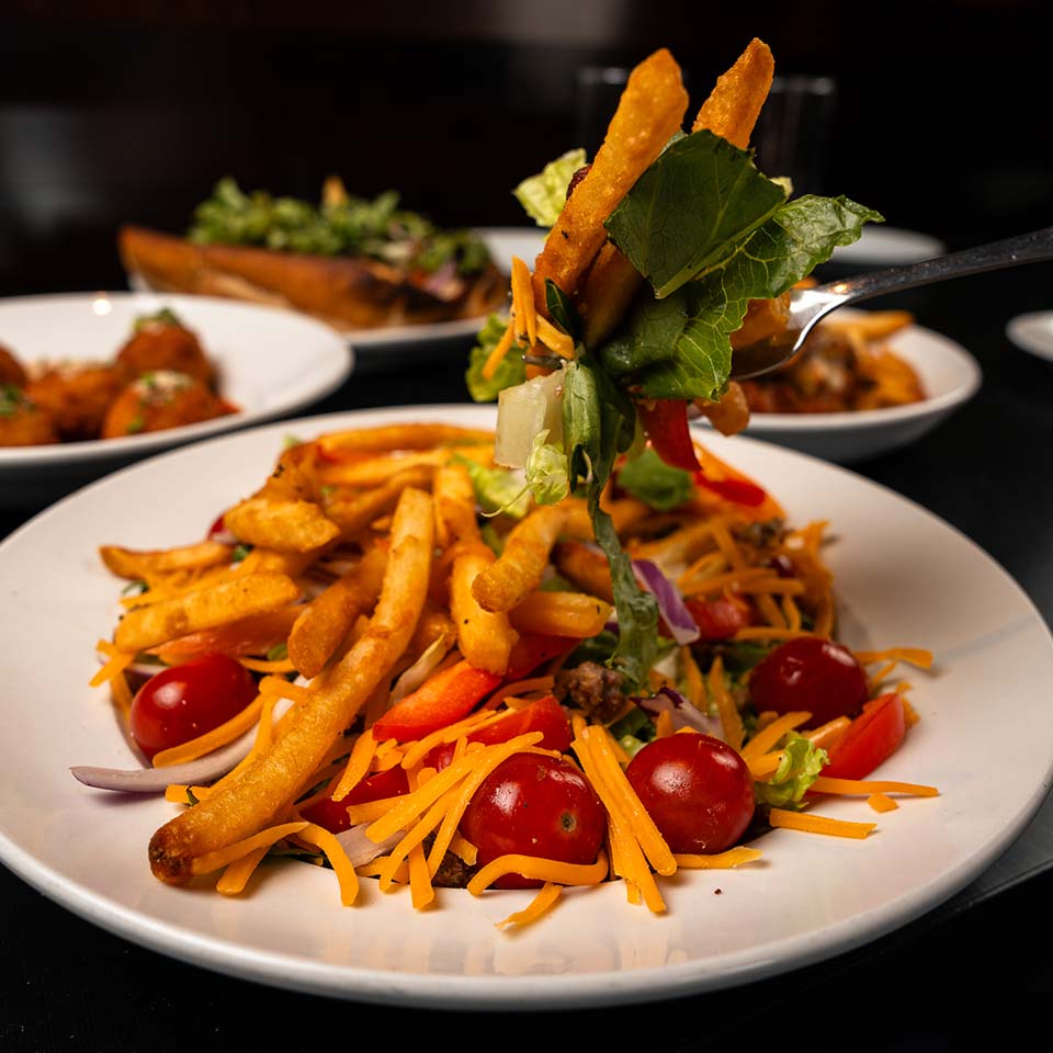 Salad with French fries, cherry tomatoes, and cheddar at DeBlaze at 131 on a white plate.