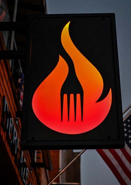 A glowing sign with a fork in an orange-red flame, perfect for a steakhouse or Italian bar.