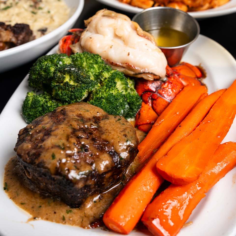 Steak with sauce, lobster tail, veggies on a white plate at DeBlaze at 131 Italian Bar.